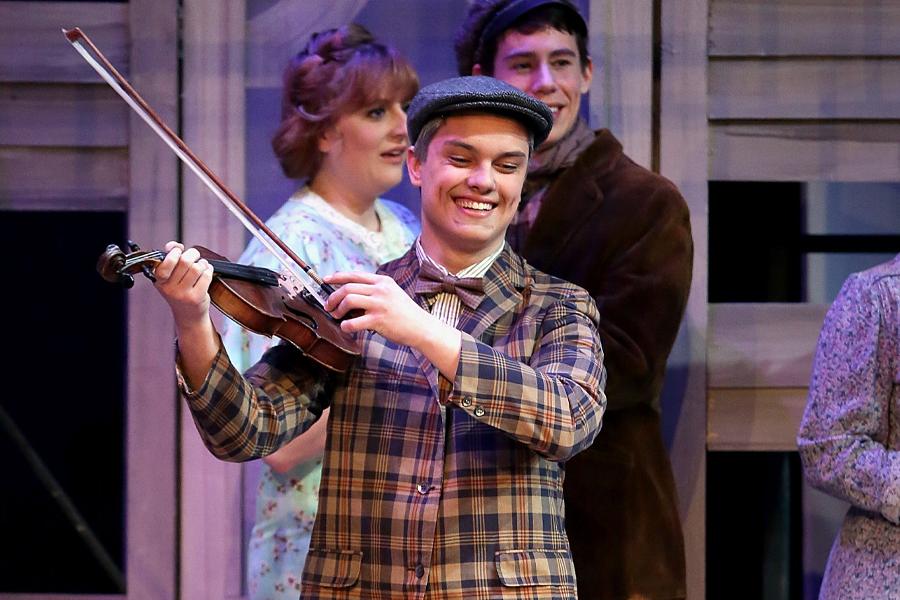 A student plays the violin on stage during a theatre performance.