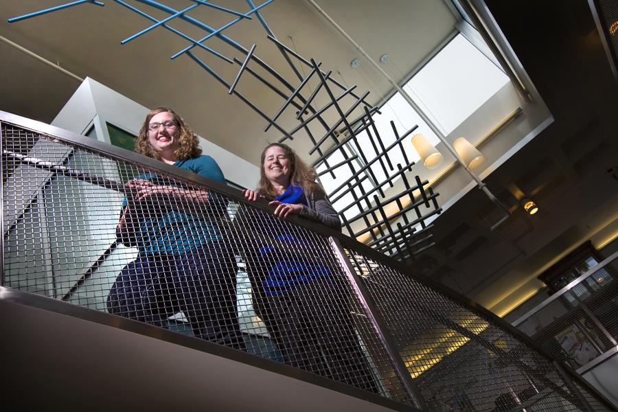 Two students stand on a staircase, smiling at the camera.