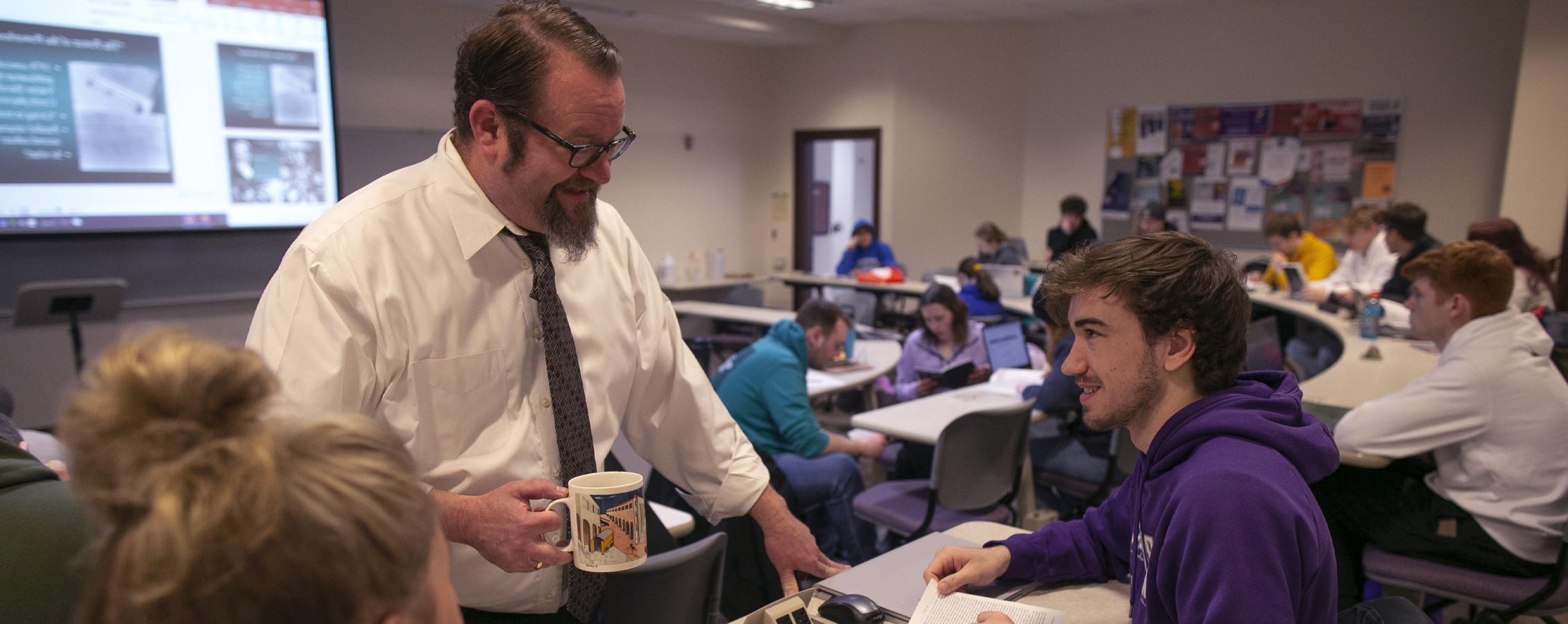 A professor visits with a student in class.