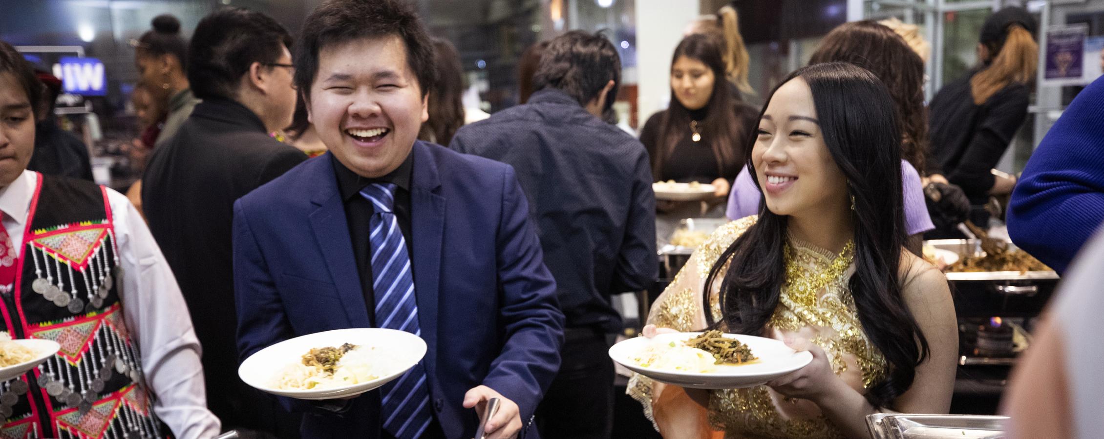 Two international students laugh together as they get food from a buffet.