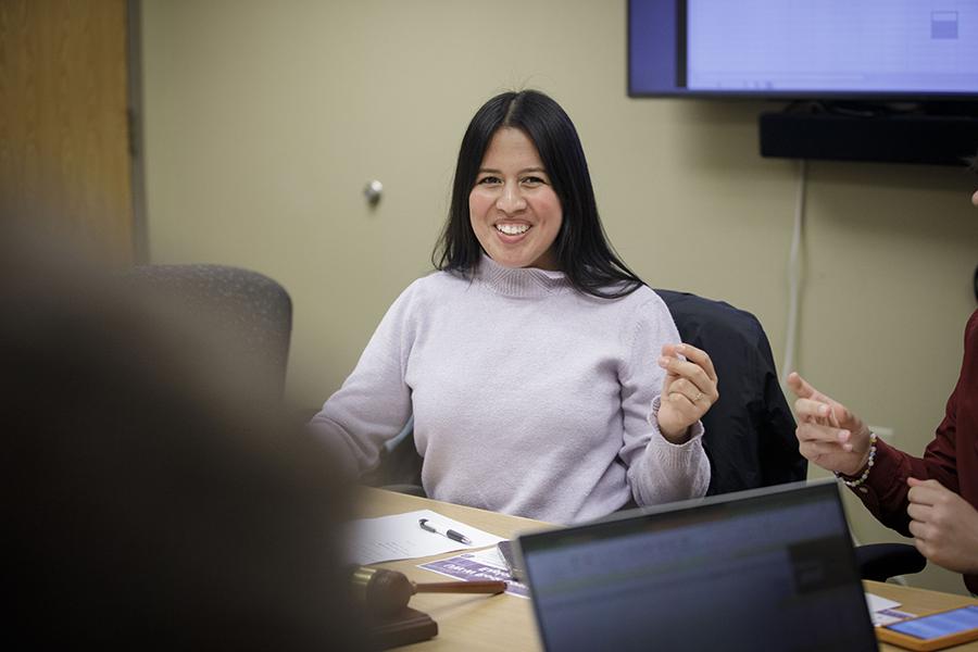 Maria Pacheco sits at a table with a smile on her face.