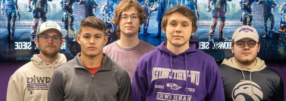 Members of the Rainbow Six: Siege Varsity Esports team standing in front of a poster