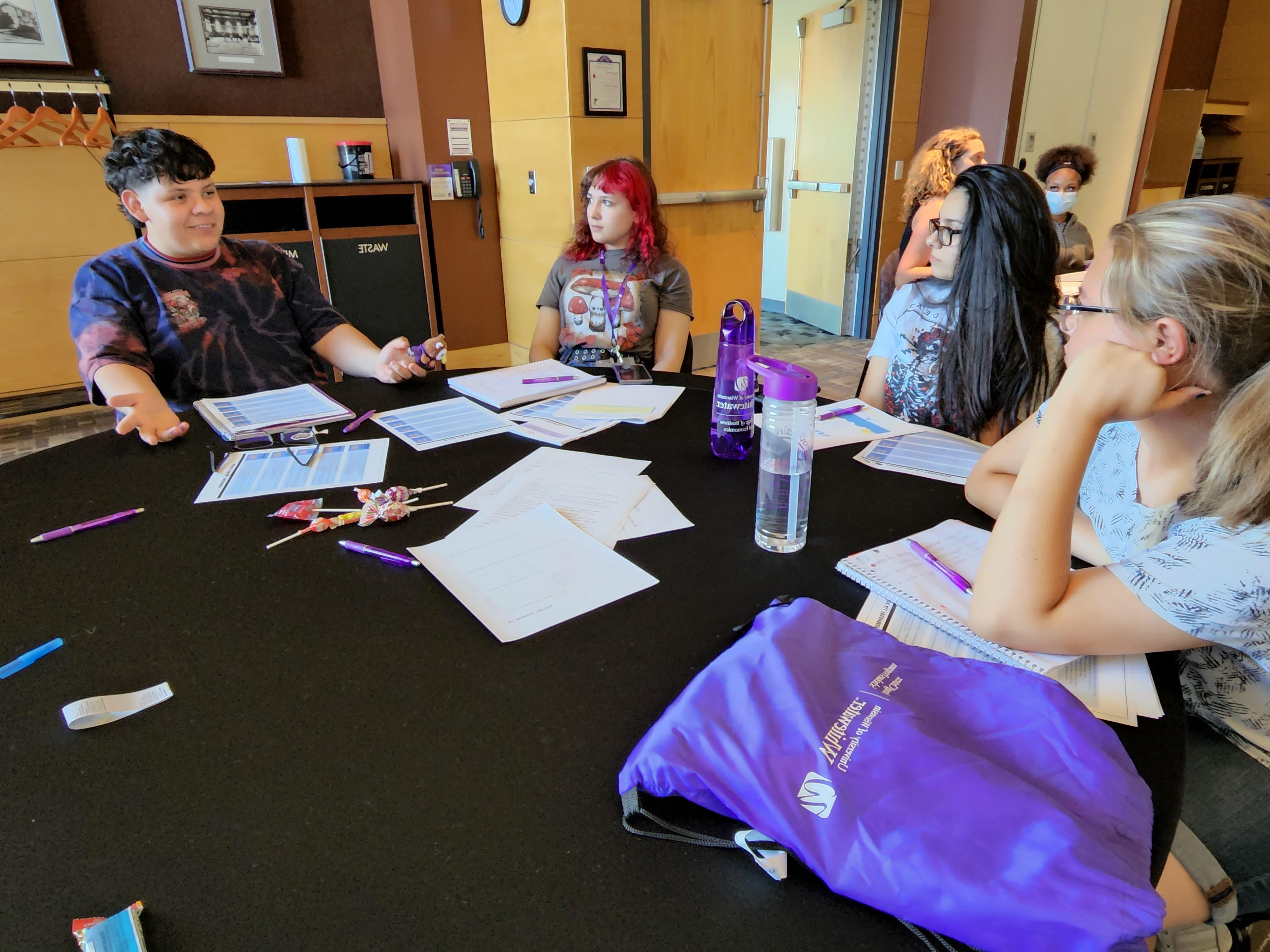 Students a faculty member sit in a circle with papers on the table.